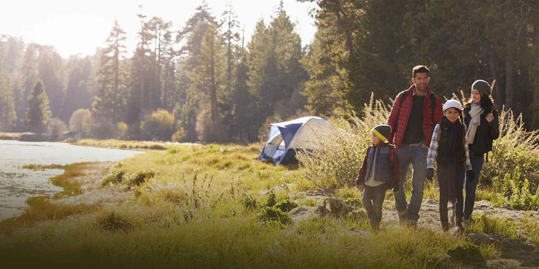 A family walks away from their tent, which is situated beside a forest and a secluded river.