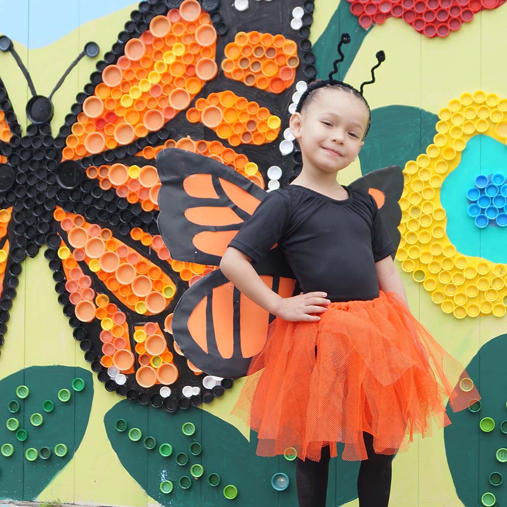 Young girl dressed as monarch butterfly in front of monarch wall art