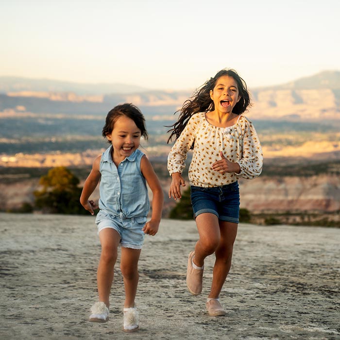 Two sisters run happily on a rugged rock landscape in Western Colorado near Fruita.