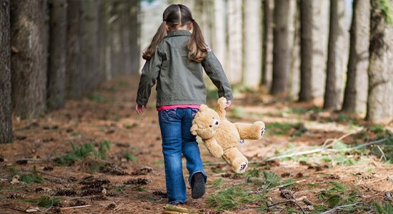 Little girl walking through forest with stuffed bear