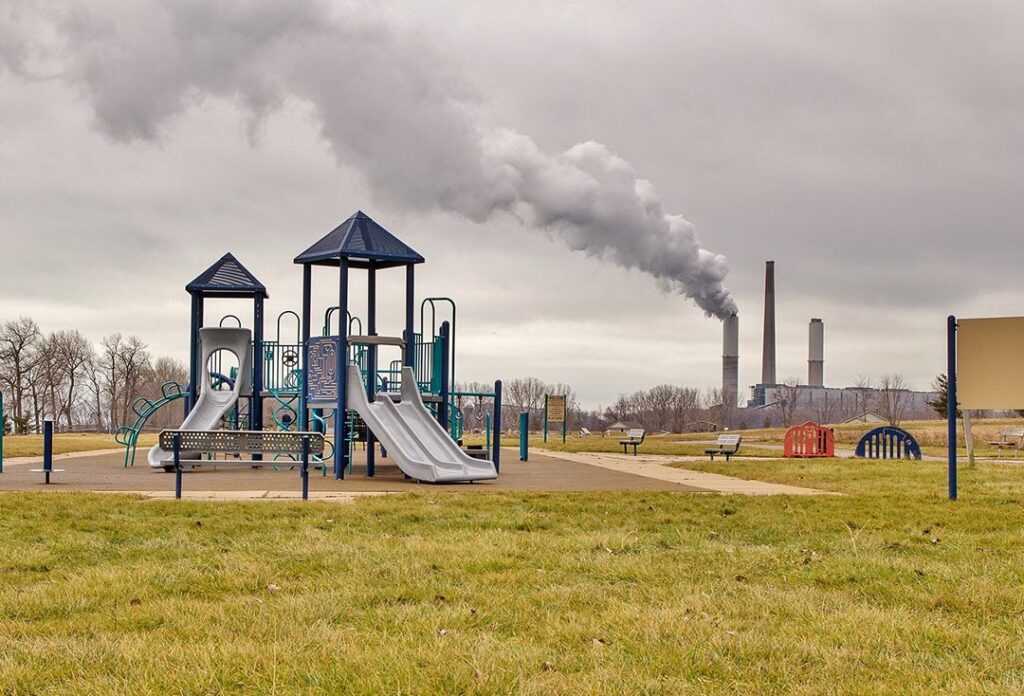 Playground With Factory Smokestack Billowing Pollution In The Background