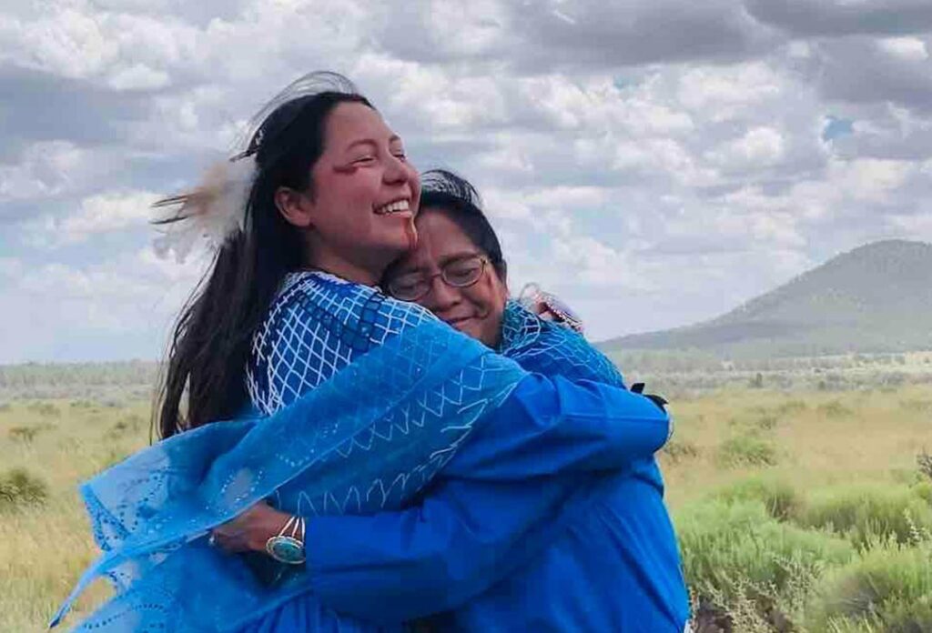 Two tribal women hug against the backdrop of the Grand Canyon