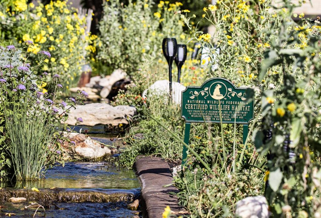 A Certified Wildlife Habitat sign is placed in the middle of garden full of flowering plants.