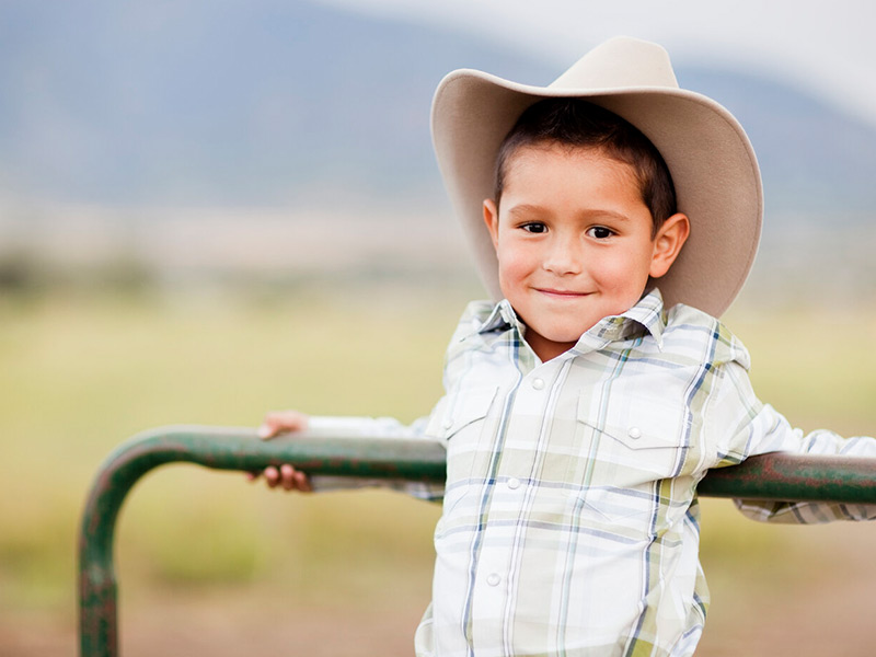 Little boy standing on a gate with a cowboy hat on