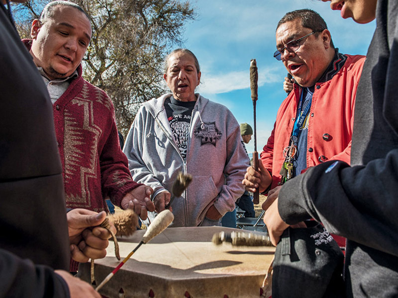 Group of five men banging on a drum and chanting outside