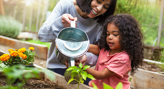 Child working in garden with adult, watering a plant