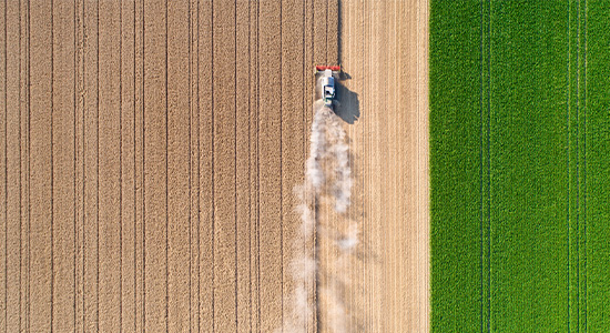 Bird's eye view of tractor driving through large field of crops